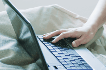 Laptop on bedding with hand resting on keyboard.